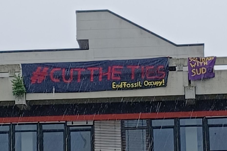 In Regen und Wind hängen zwei Banner vom Dach des GW2, einem markanten Gebäude der Universität Bremen im Stil des Brutalismus. Auf den Bannern steht "Cut the ties! EndFossil: Occupy" und "Solidarity with Sudan" (das "a" im Wort Sudan ist ein Anarchie-A).